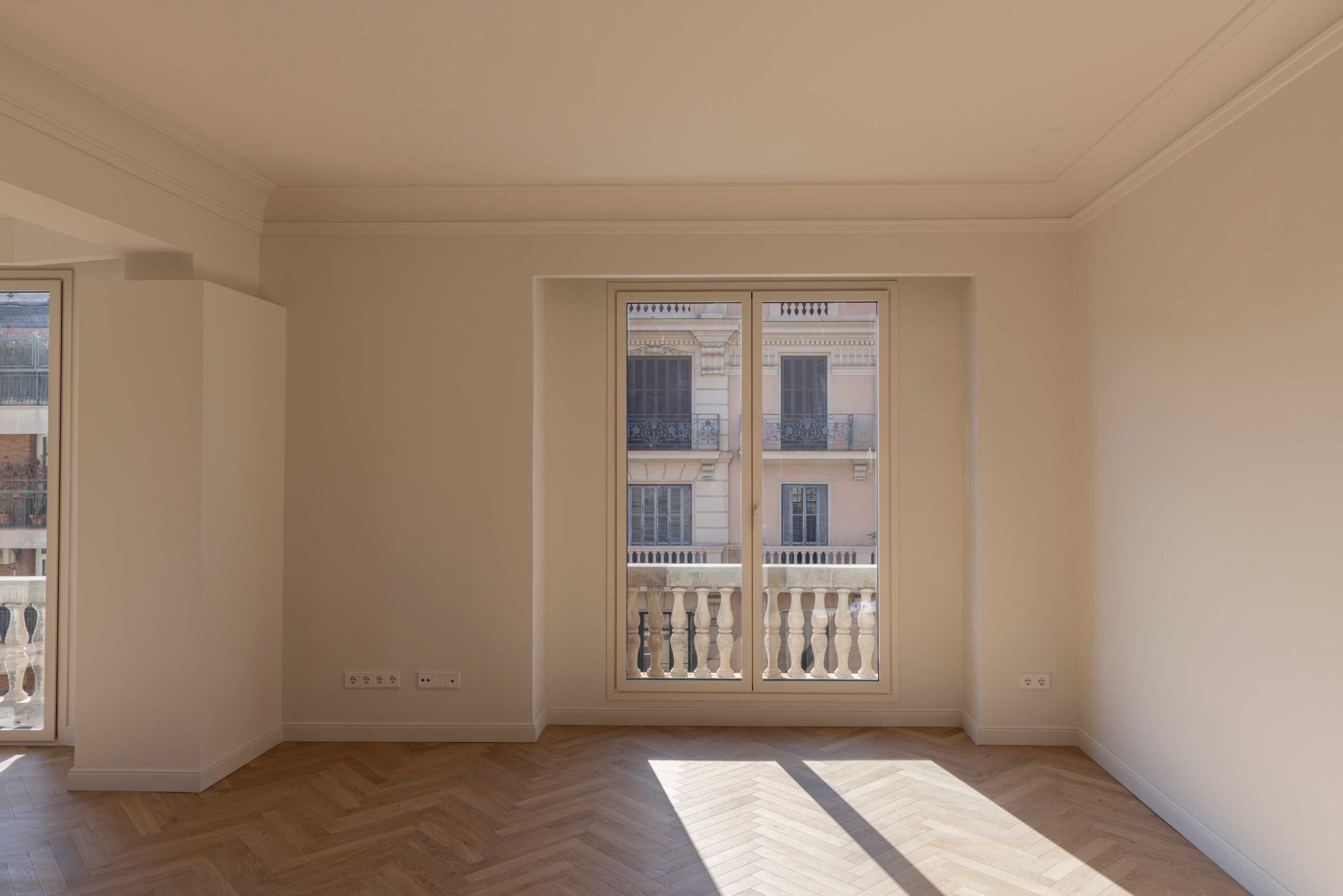 Zona de día con parquet en espiga y luz natural en un piso reformado de Barcelona